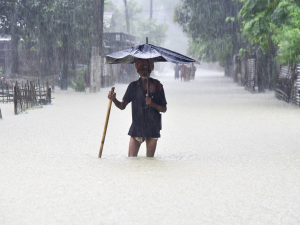 Un vecchio uomo cammina per le strade allagate del villaggio di Nalbari (Assam India) con un ombrello rotto
