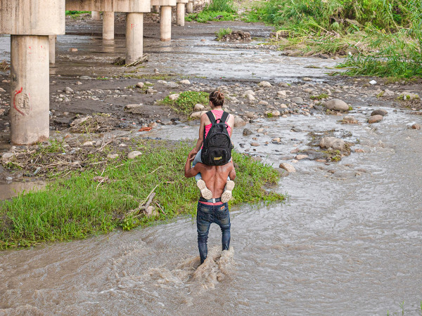 Un hombre carga a una mujer sobre sus hombros mientras cruza el río Táchira en la frontera entre Venezuela y Colombia.