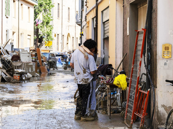 Faenza (Ravenna, Emilia-Romagna, Italia). Una giovane coppia sporca di fango si bacia tra detriti e pile di oggetti recuperati dall’alluvione
