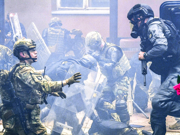 Un ufficiale di polizia del Kosovo salta fuori da un veicolo blindato mentre i soldati della forza internazionale per il mantenimento della pace del Kosovo (Kfor), guidata dalla Nato, giacciono feriti dopo una colluttazione con serbi davanti all'edificio del Comune di Zvecan, il 29 maggio 2023