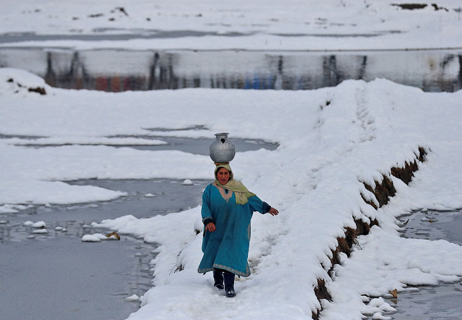 Kashmir, 9 gennaio 2022. Una donna porta con maestria una brocca d’acqua sul capo attraverso un campo innevato alla periferia di Srinagar.