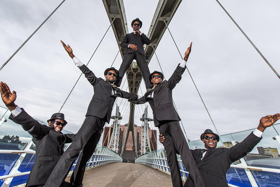 Salford (Gran Bretagna). Il gruppo teatrale e circense ‘The Black Blues Brothers’ esegue un&rsquo;acrobazia sul Millennium Bridge a Salford Quay (EPA/ADAM VAUGHAN)