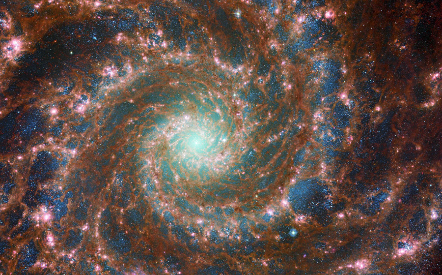 Un’immagine inedita della Galassia Fantasma M74, frutto della collaborazione tra i telescopi spaziali James Webb e Hubble. La galassia, appartenente alla classe delle galassie a spirale “grand design” in virt&ugrave; dei suoi bracci prominenti e ben definiti, si trova a circa 32 milioni di anni luce dalla Terra nella costellazione dei Pesci.