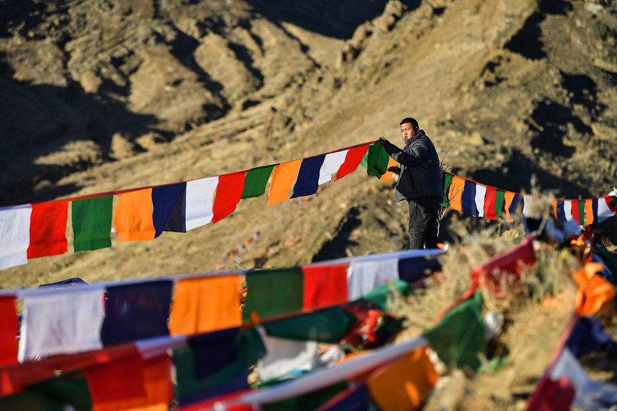 Xigaze (Cina). Un uomo appende delle bandiere su una montagna, nella regione autonoma del Tibet, per celebrare il nuovo anno del calendario tibetano: molti l&rsquo;hanno fatto, in segno di preghiera, anche sui tetti delle loro case. 