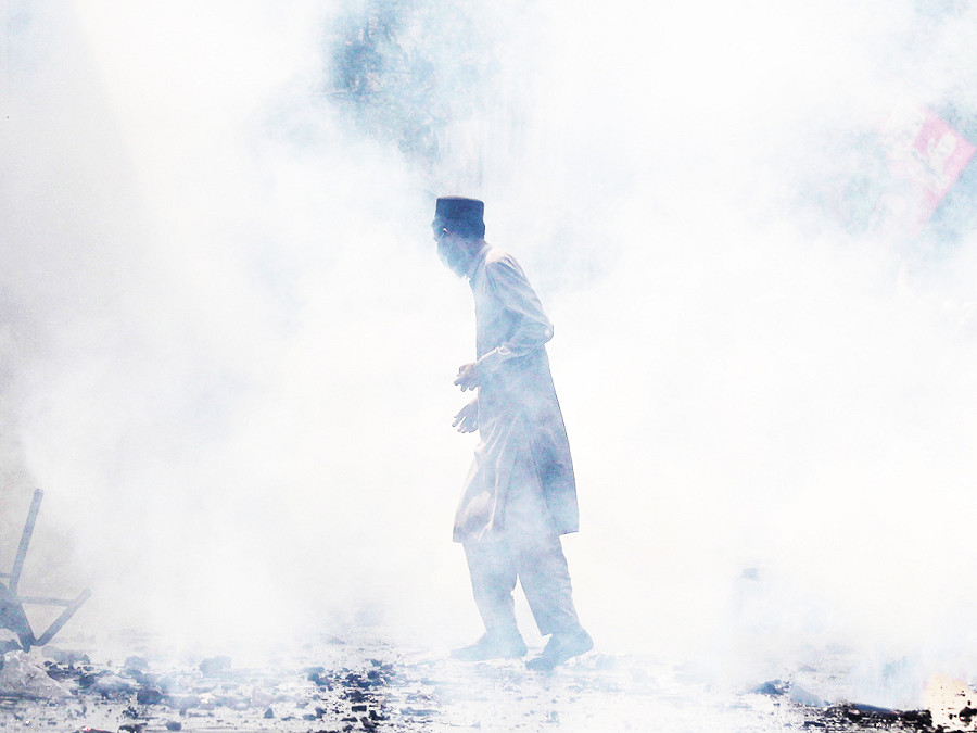 Lahore (Pakistan). Un cittadino pakistano cammina tra i gas lacrimogeni durante gli scontri tra la polizia e i sostenitori dell’ex Primo ministro Imran Khan per impedirne l’arresto. Il leader dell’opposizione &egrave; accusato di non aver dichiarato diversi doni statali ricevuti da dignitari stranieri e di averli rivenduti illegalmente.