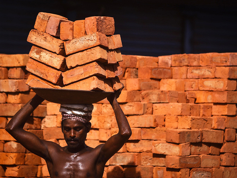 Chennai, India. Un operaio trasporta mattoni sulla testa in un complesso commerciale in costruzione. 