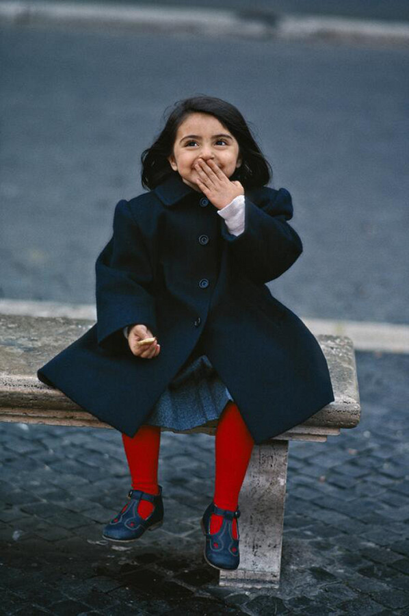 Roma (Italia). &Egrave; il 1990: una bambina con un cappotto scuro e delle calzamaglie rosse ride sotto i baffi su una panchina di Piazza Navona. A distanza di 33 anni l&rsquo;autore dello scatto, il celebre Steve McCurry, ha incontrato Mara Marcetelli nello stesso posto. E le ha regalato la sua fotografia. 