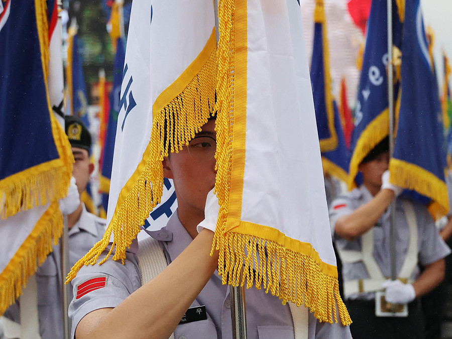 Seongnam (Corea del Sud). Un militare sudcoreano nascosto dal drappo di una bandiera marcia durante una delle celebrazioni per il 75&deg; anniversario della Giornata delle Forze Armate della Corea. Si tratta della prima parata militare su larga scala in un decennio. 