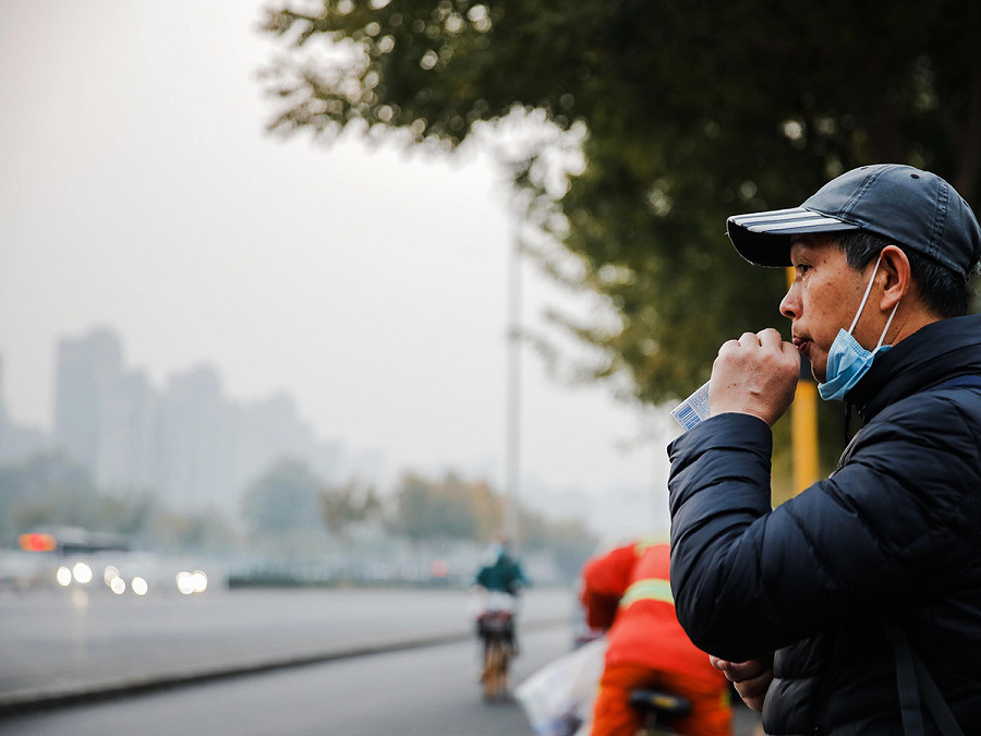 Pechino (Cina). Un uomo con una mascherina chirurgica beve ai lati di una strada, circondato dallo smog. Secondo il rapporto del Centro municipale di monitoraggio ecologico e ambientale locale, il 21 novembre l’indice di qualit&agrave; dell’aria ha raggiunto un livello di inquinamento moderato, pari a 4. 