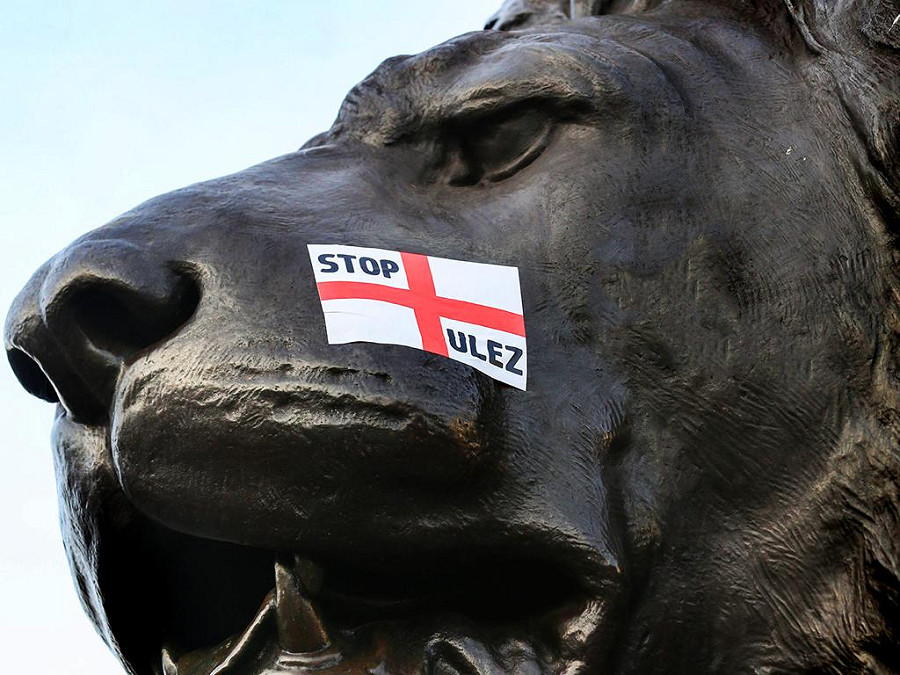 Londra (Regno Unito). Un manifestante attacca adesivi anti-ULEZ sul leone di Trafalgar Square, durante la manifestazione di protesta organizzata a un anno di distanza dall’introduzione dell’Ultra-Low Emission Zone nella capitale britannica. 