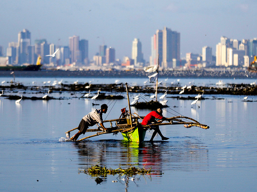 Bacoor (Filippine). Due pescatori spingono una barca lungo la baia di Manila. Secondo le previsioni dell’Ufficio filippino per la pesca e le risorse acquatiche, il calore portato dal fenomeno El Ni&ntilde;o provocher&agrave; un abbassamento del livello delle acque, con la crescita della mortalit&agrave; dei pesci.
