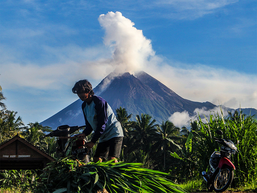 Sleman (Indonesia). Mentre un contadino si prende cura della sua risaia, dal Monte Merapi in lontananza fuoriesce fumo vulcanico. Le autorit&agrave; hanno emesso lo stato di allerta da quando, questo luned&igrave;, il vulcano ha iniziato a emettere nuvole di fumo caldo. 