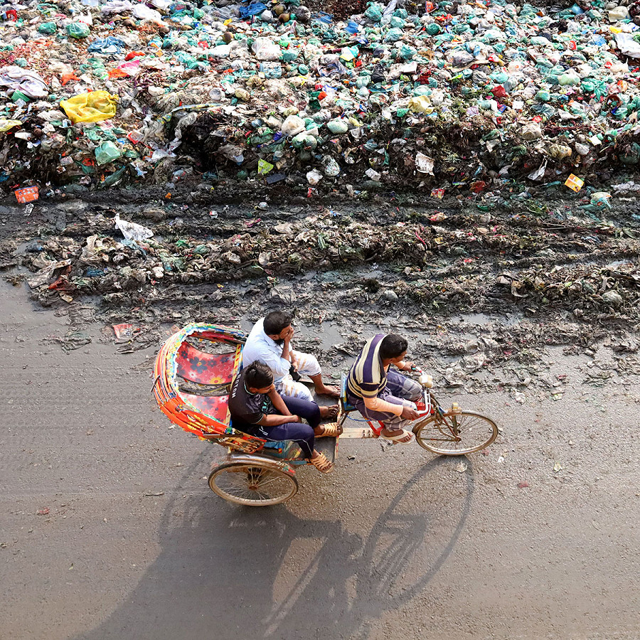 Narayanganj (Bangladesh). Un risci&ograve; a due posti trainato da un uomo passa accanto a dei rifiuti accumulati a lato della strada. Oltre all’inquinamento ambientale, l&rsquo;immondizia provoca anche ingorghi sulle strade. 