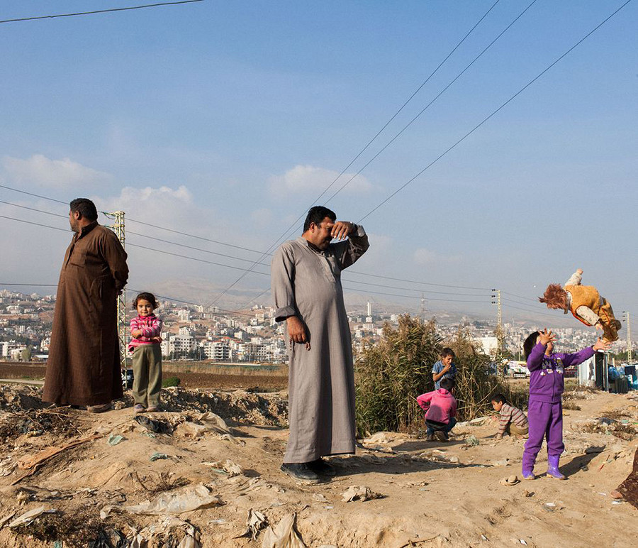Beqaa, Libano. Rifugiati siriani che vivono a Fayda, insediamento di tende nella valle della Beqaa in Libano, stanno in piedi, fuori dalle loro baracche, di fianco a un canale di acqua inquinata