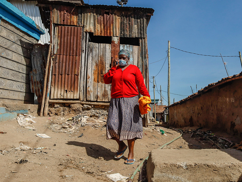 A woman wearing a face mask walks past the local neighborhood's in Kibera Slums, Nairobi. Life is a little surprising due to the extreme level of happiness from the community despite the high rate of poverty and lack of jobs