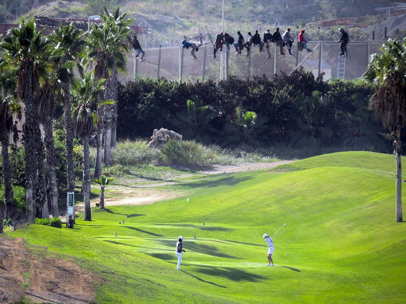 Nello scatto di José Palazón tratto dal profilo twitter dell'organizzazione umanitaria Prodein, il contrasto di una città di frontiera come Melilla. Sulla rete che circonda la città sono rimasti in bilico, per più di 12 ore, circa settanta migranti che hanno cercato di superare la barriera. A pochi passi dalla loro disperazione, gli abitanti di Melilla hanno continuato a giocare sui campi da golf