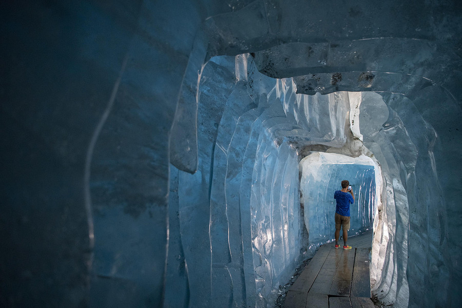 Un visitatore esplora una grotta di ghiaccio del ghiacciaio alpino del Rodano, all'estremità nord-est del Canton Vallese in Svizzera. È il più antico delle Alpi: oggi è protetto da speciali coperte bianche per scongiurarne lo scioglimento