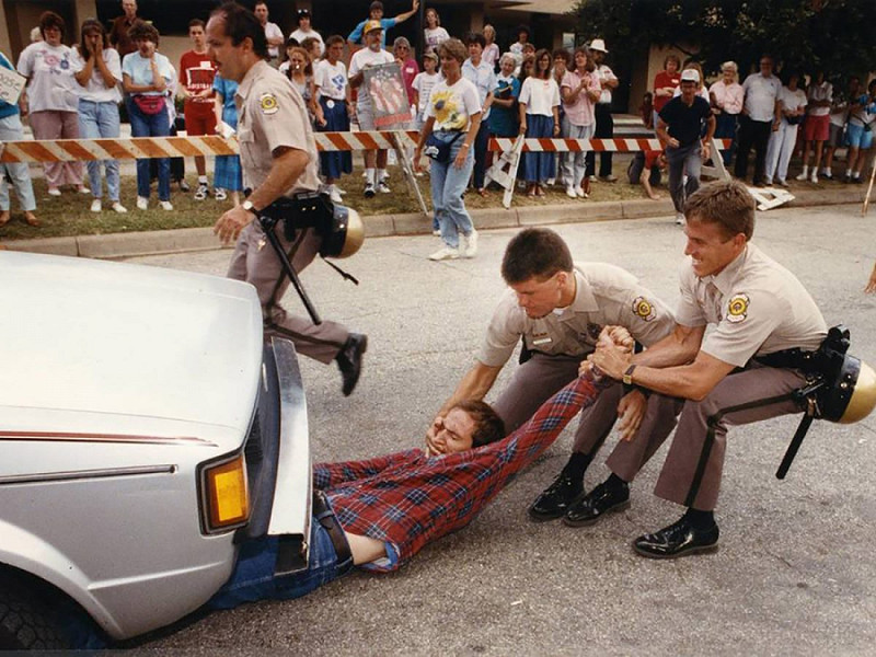Alcuni agenti di polizia di Wichita, in Kansas, tentano di rimuovere una manifestante abortista da sotto un'auto all'ingresso della clinica del dottor George Tiller durante la protesta Summer of Mercy del 1991. 