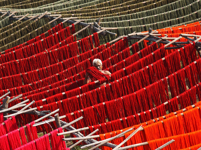 An Indian laborer hangs dyed yarn for drying under the sun